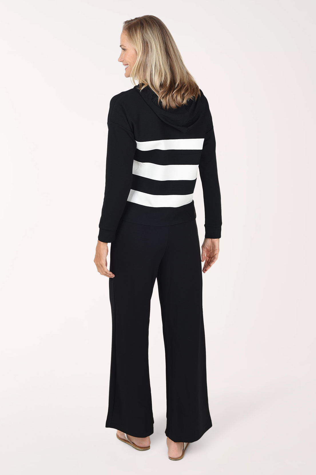 A woman wearing a black/white striped long-sleeve hooded top and matching black pants, standing against a plain white studio background.