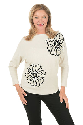 Woman wearing a cream sweater with black floral designs on a white background.