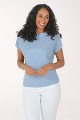 Woman wearing a blue textured top and white pants on a light background