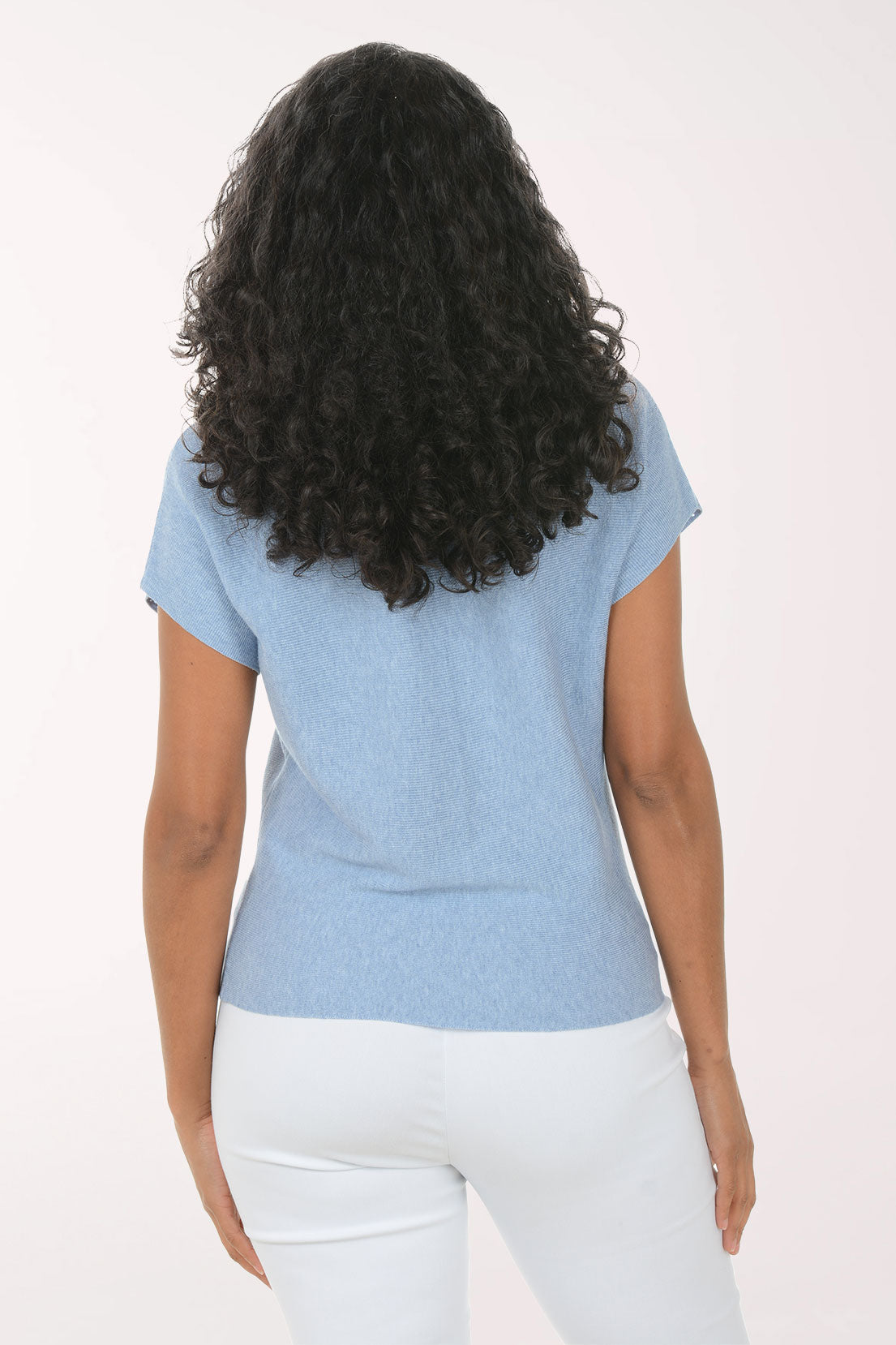 Woman wearing a blue textured top and white pants on a light background