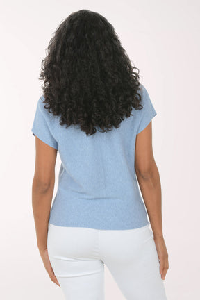 Woman wearing a blue textured top and white pants on a light background