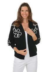 Woman wearing a black cardigan with white floral patterns on a white background.