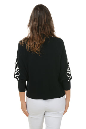 Woman wearing a black cardigan with white floral patterns on a white background. Back shot.