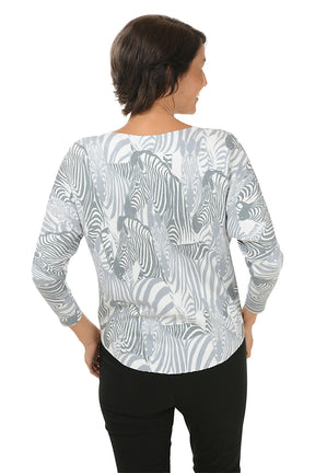 Woman wearing a grey and white zebra illustrated patterned long-sleeve top on a white background.  Back shot.