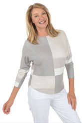 Woman wearing a gray and white patterned top with white pants on a white background.