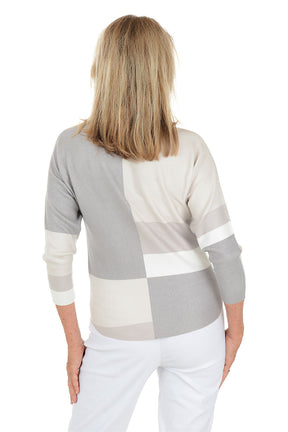 Woman wearing a gray and white patterned top with white pants on a white background. Back shot.