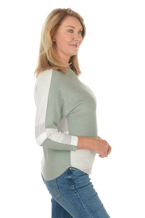 Woman wearing a color-blocked sweater with green and white sections on a white background. Side shot.