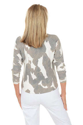 Woman wearing a gray and white cow patterned sweater with white pants on a white background. Back shot.