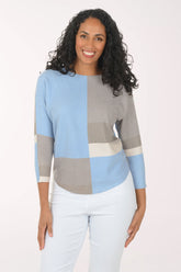 Woman wearing a color-blocked sweater with blue, gray, and beige sections on a white background.