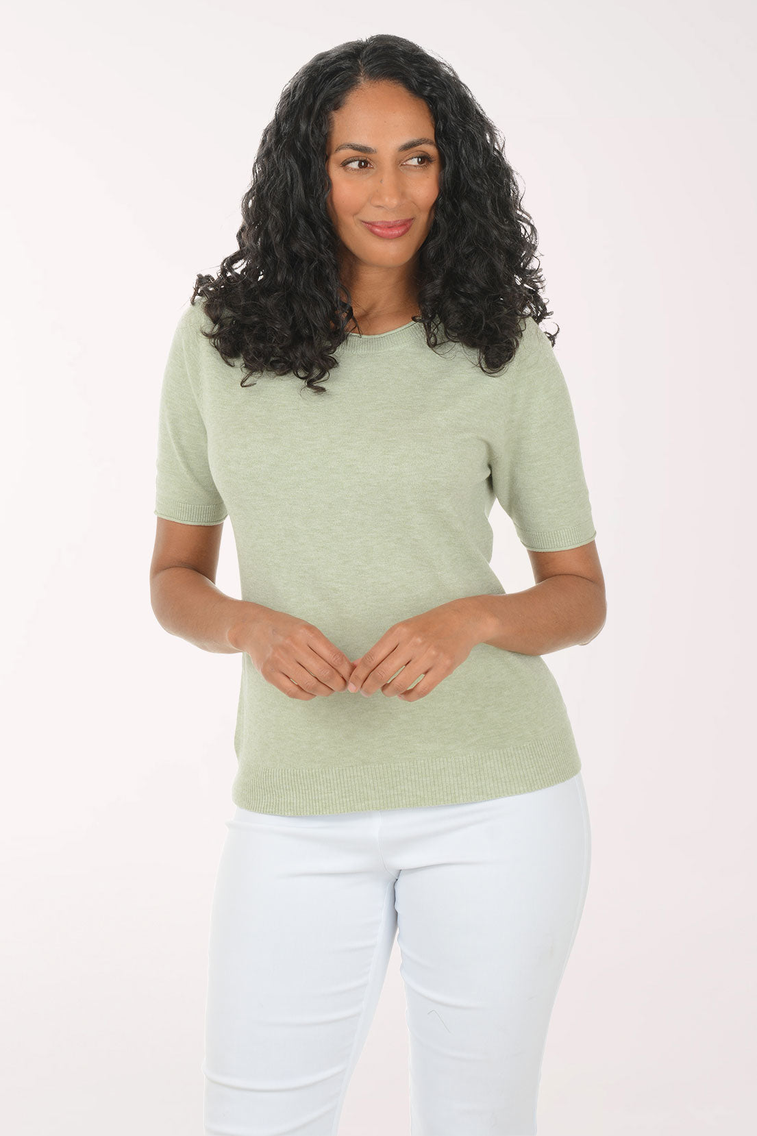 Woman wearing a green top and white pants on a light background
