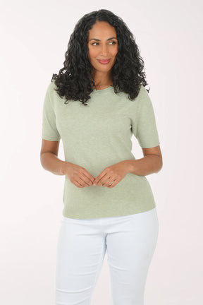 Woman wearing a green top and white pants on a light background