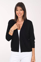 Front view of a model wearing the Milano Waffle Knit Open Cardigan in black, a cropped open-front cardigan with 3/4 raglan sleeves, layered over a white tank with white pants.
