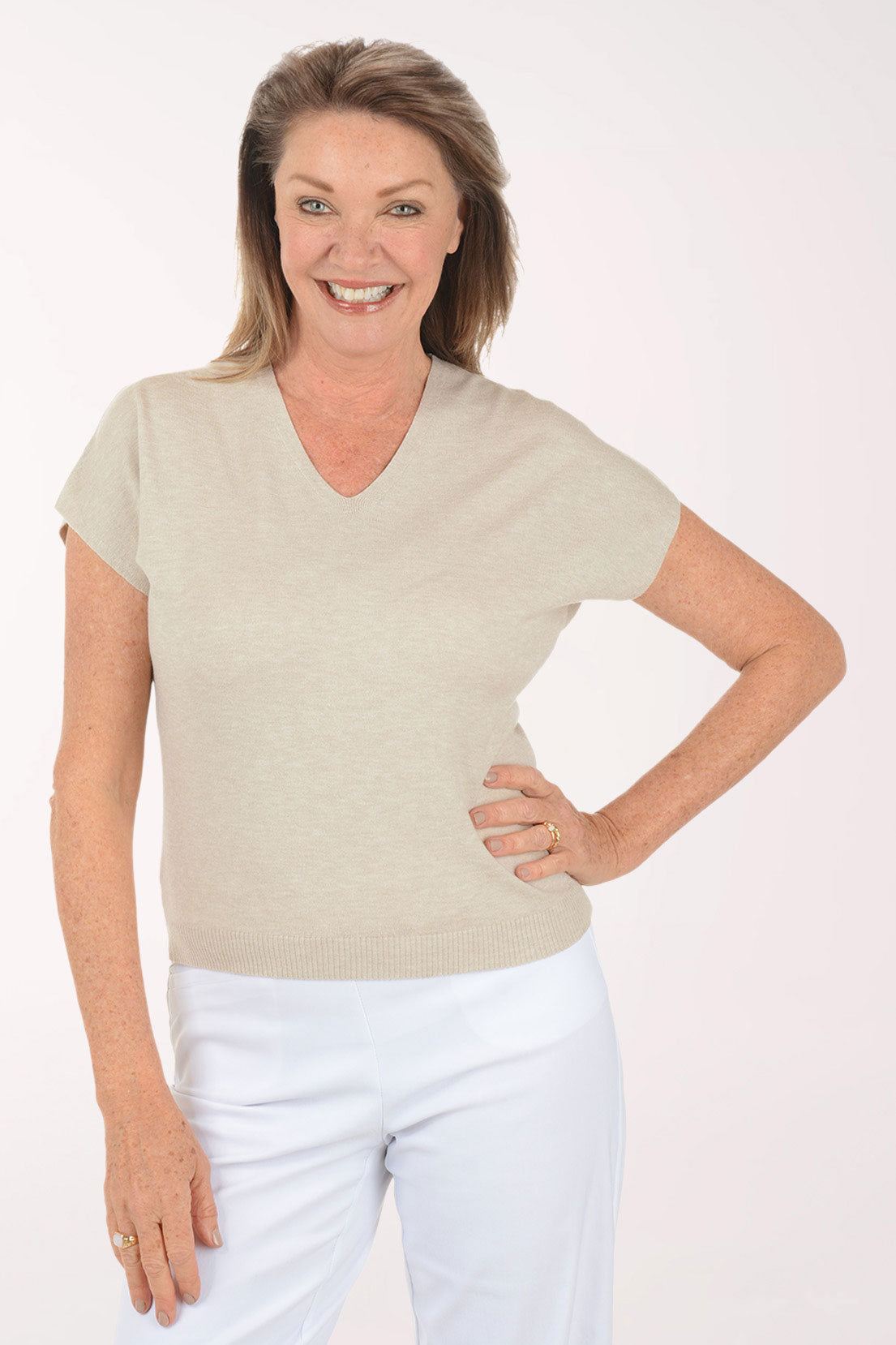 Woman wearing a beige top and white pants on a white background