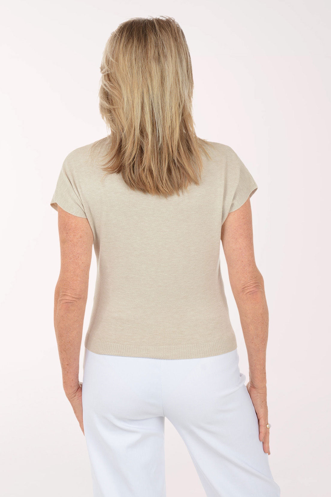 Woman wearing a beige top and white pants on a white background