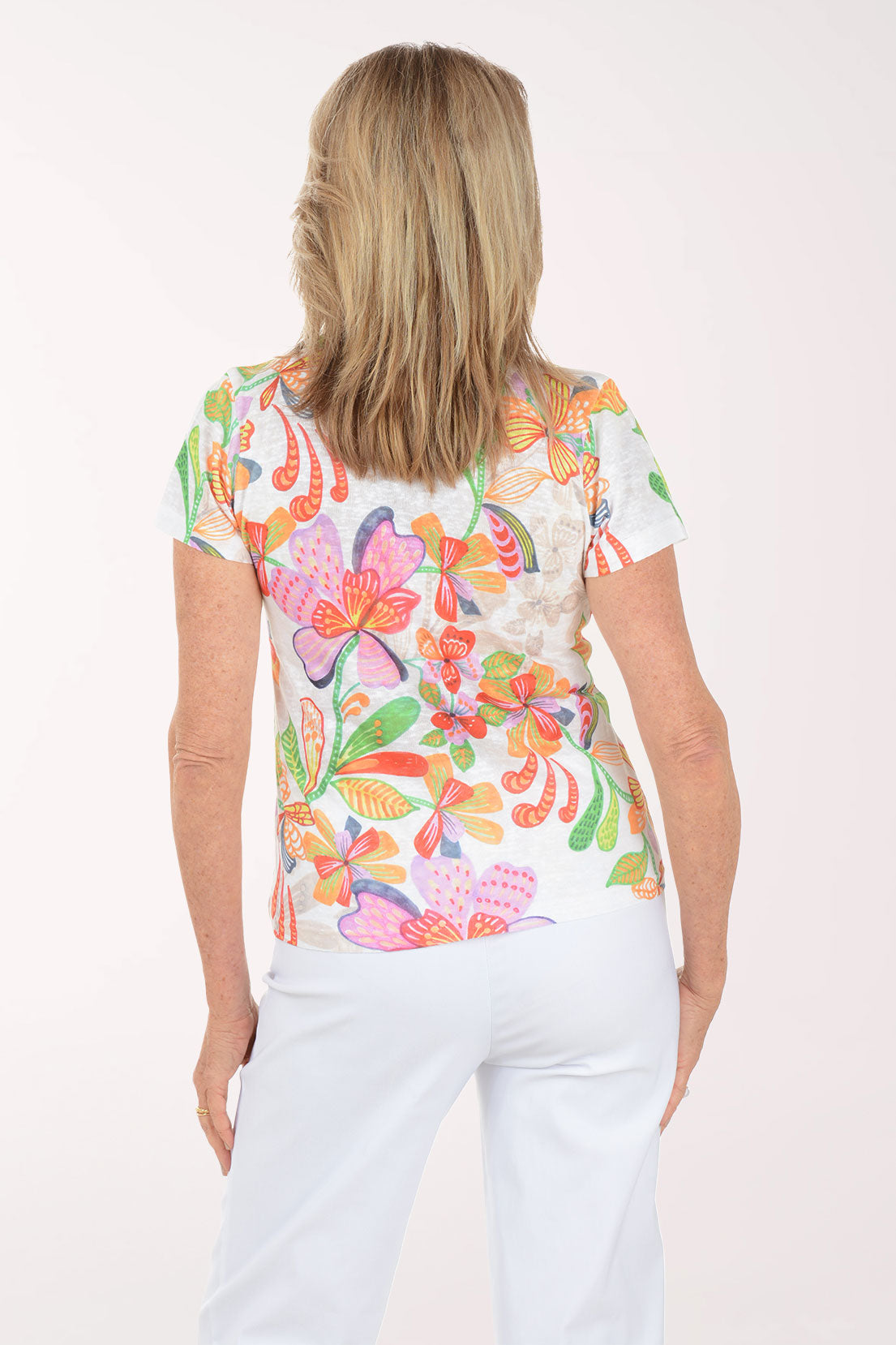 Woman wearing a colorful floral top and light blue pants on a white background