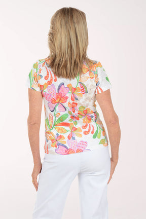 Woman wearing a colorful floral top and light blue pants on a white background