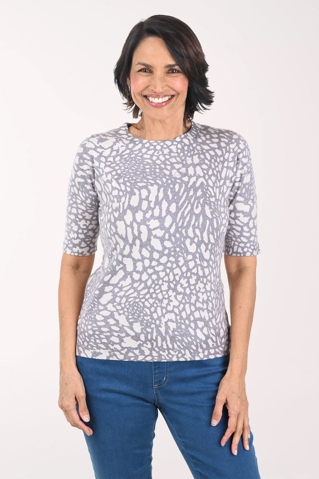 Woman wearing a patterned gray sweater and blue jeans on a white background