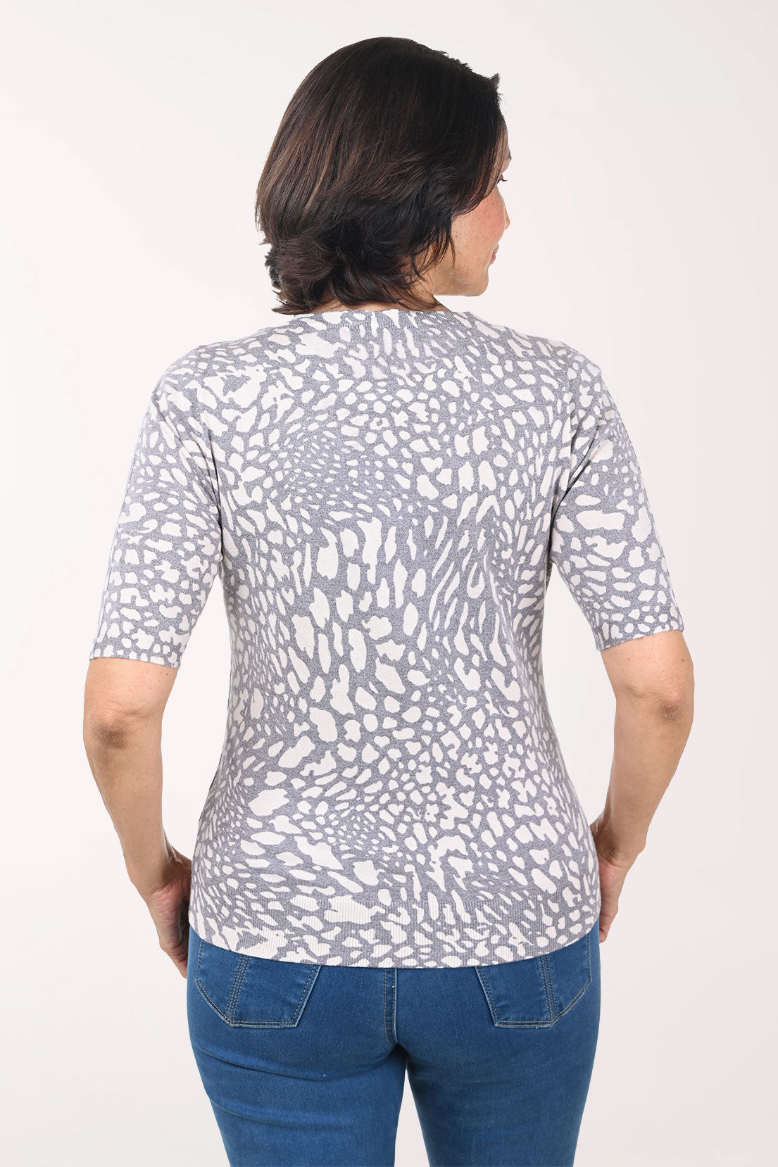 Woman wearing a patterned gray sweater and blue jeans on a white background