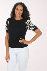 Woman wearing a black top with floral embellishments on sleeves against a white background