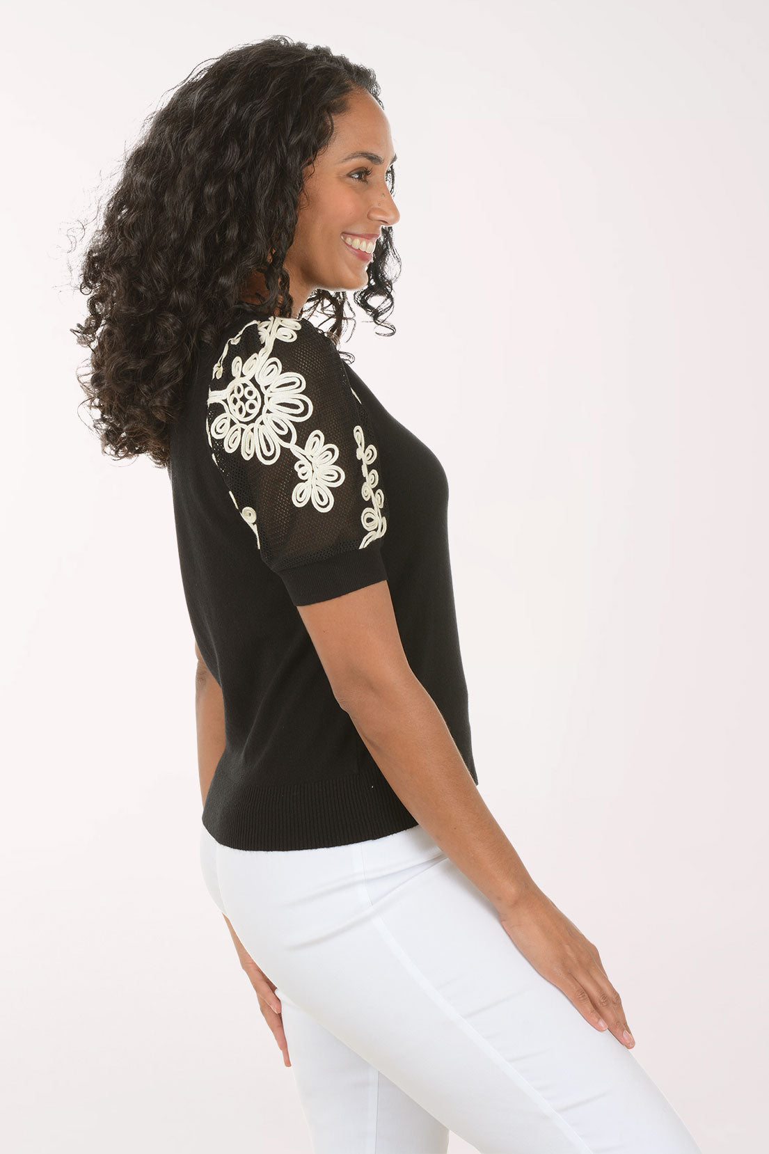 Woman wearing a black top with floral embellishments on sleeves against a white background