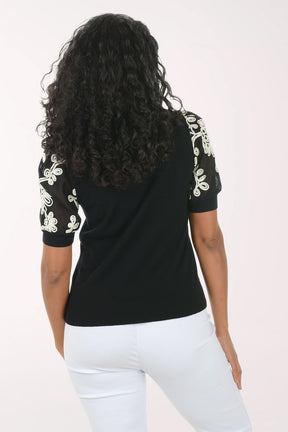 Woman wearing a black top with floral embellishments on sleeves against a white background