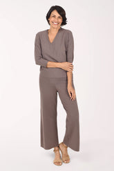 A woman modeling a taupe knit matching set with three-quarter sleeves and wide legs, paired with beige heeled sandals, against a plain white studio background.