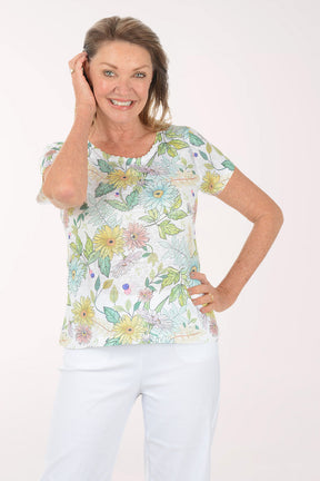 Woman wearing a floral print top and white pants on a white background