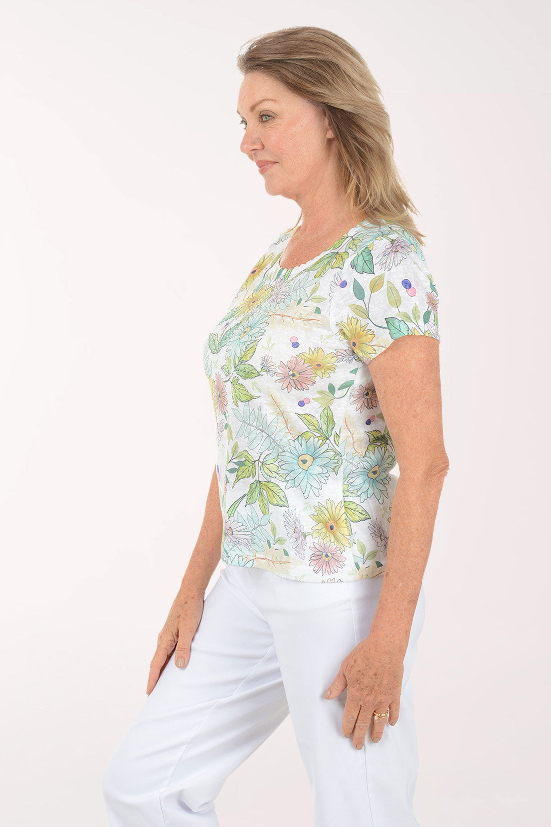 Woman wearing a floral print top and white pants on a white background