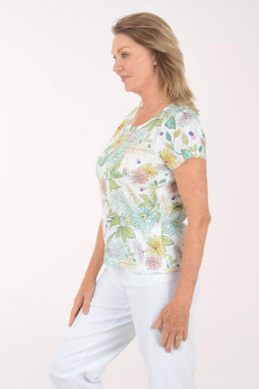 Woman wearing a floral print top and white pants on a white background