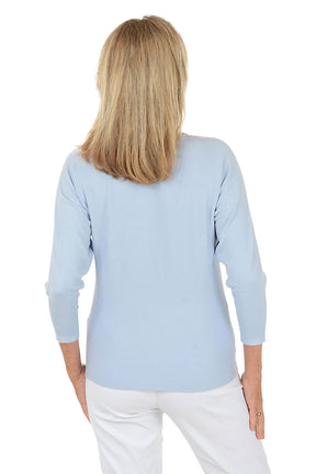 Woman wearing a light blue sweater with a flower design on a white background. Back shot.