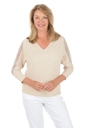 Woman wearing a beige sweater with peekaboo cutouts on the shoulders, layered with rhinestone-embellished sheer mesh fabric on a white background.