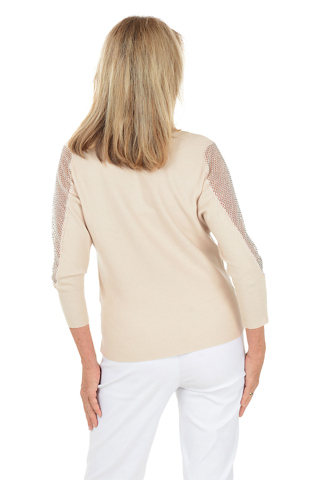 Woman wearing a beige sweater with peekaboo cutouts on the shoulders, layered with rhinestone-embellished sheer mesh fabric on a white background. Back shot.