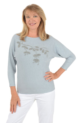 Woman wearing a light blue sweater with silver floral embroidery on a white background.