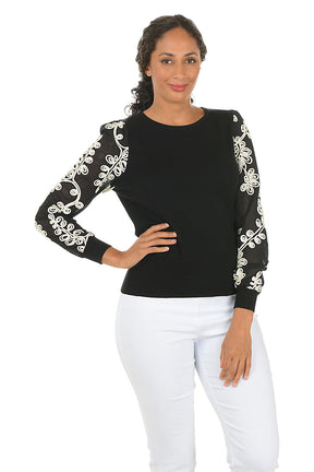 Woman wearing a black top with white embroidery on sleeves against a white background.