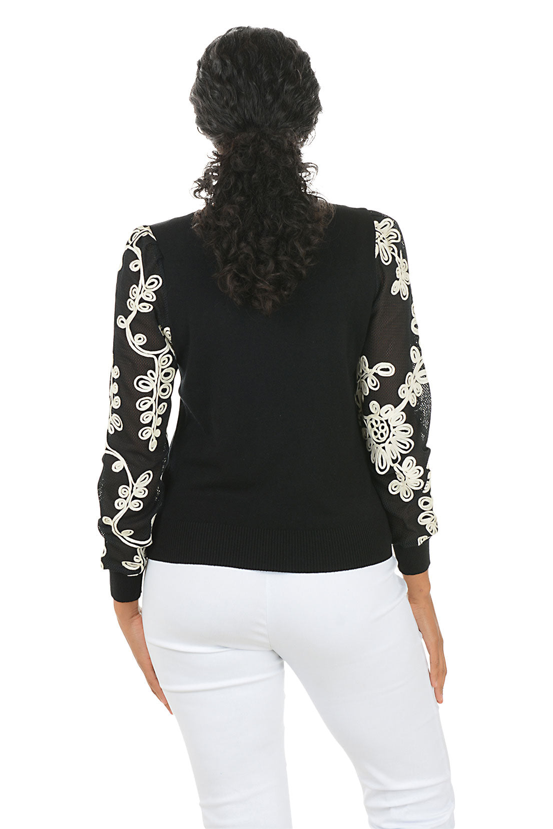 Woman wearing a black top with white embroidery on sleeves against a white background. Back shot.