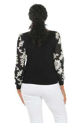 Woman wearing a black top with white embroidery on sleeves against a white background. Back shot.