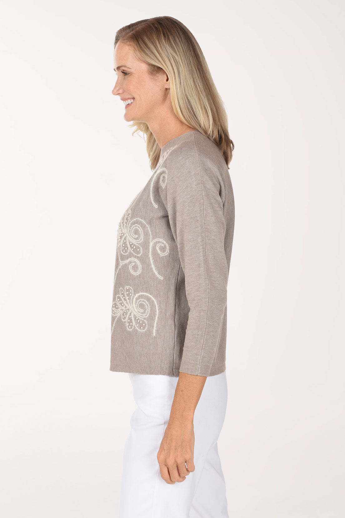 Woman wearing a beige 3/4 sleeve sweater with a white pearl flower design 