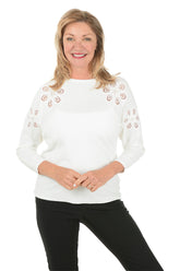 Woman wearing a white sweater with decorative cut-out patterns on a white background.