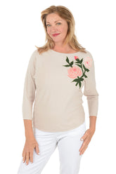 Woman wearing a beige sweater with floral embroidery on a white background.
