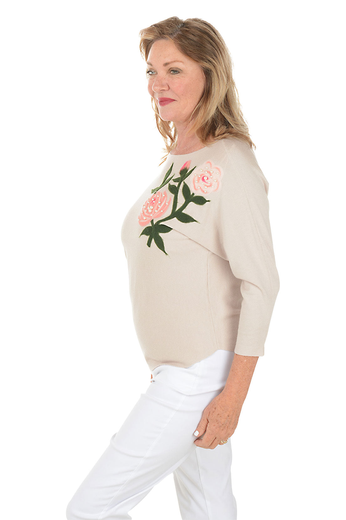 Woman wearing a beige sweater with floral embroidery on a white background. Side shot.