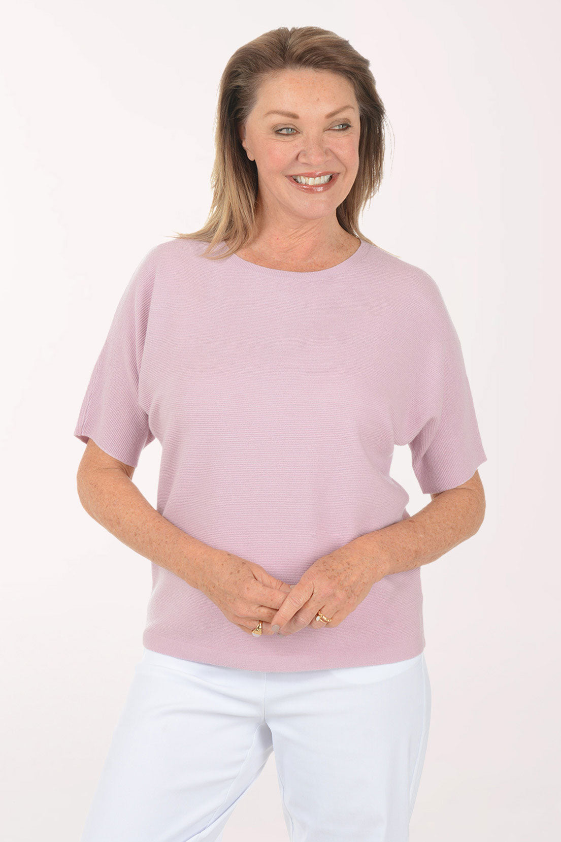 Woman wearing a pink top and white pants on a light pink background