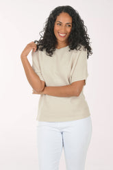 Woman wearing a beige top and white pants on a white background