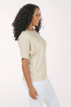 Woman wearing a beige top and white pants on a white background