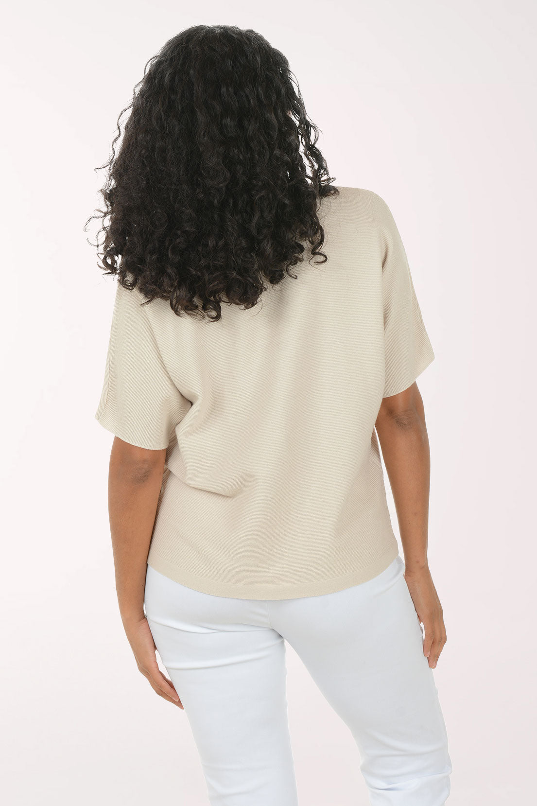 Woman wearing a beige top and white pants on a white background