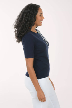 Woman wearing a navy blue top with a patterned neckline against a light pink background