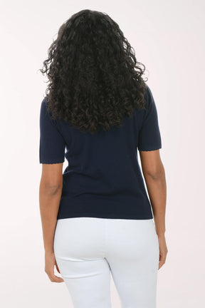 Person wearing a navy blue t-shirt and white pants on a light pink background