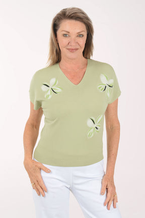 Woman wearing a light green sweater with dragonfly designs on a white background
