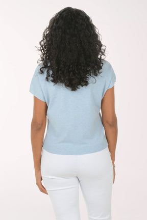 Woman wearing a light blue t-shirt with white butterfly designs on a plain background