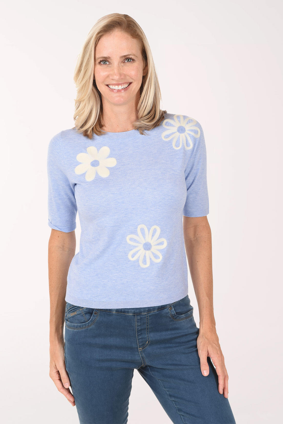 Woman wearing a light blue sweater with white flower designs on a white background