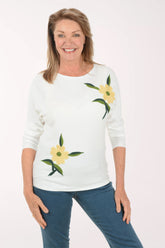 Woman wearing a white sweater with floral designs on a plain background